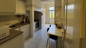 A modern kitchen with white cabinets, a granite countertop, and a dining area with a white table and chairs. - Terrace Marquês (Lisbon)