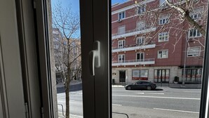 A window view of a street with a building, a tree, and a parked car. - Terrace Marquês (Lisbon)