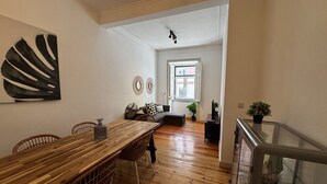 A spacious dining area with a wooden table and wicker chairs, a living room with a sofa and a window, and a staircase leading to an upper level. - Terrace Marquês (Lisbon)