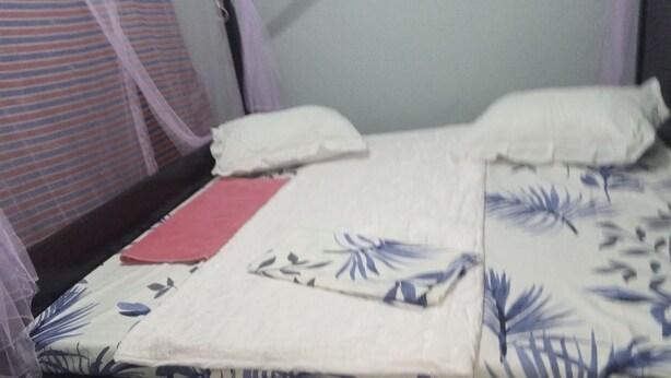 Una cama con una colcha estampada con flores, un cojín rojo y cojines blancos.