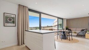 Una cocina moderna con una isla grande, un comedor con mesa redonda y vistas a un edificio de la calle.