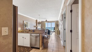 A kitchen with a central island, a dining area, and a view to the outside. - Emerald Isle 403 (Panama City Beach)