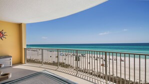 A balcony with a view of a beach, a sun decoration on the wall, and a small seating area with a rug. - Emerald Isle 403 (Panama City Beach)