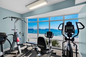 Une salle de sport équipée de machines de cardio-training et offrant une vue sur la plage.