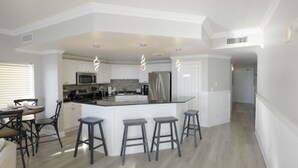 Una cocina moderna con armarios blancos, una isla central con taburetes, un refrigerador de acero inoxidable y un microondas.
