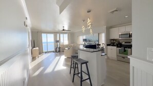 Amplia sala de estar con un gran ventanal, un sofá, una mesa de centro y una cocina con electrodomésticos modernos.