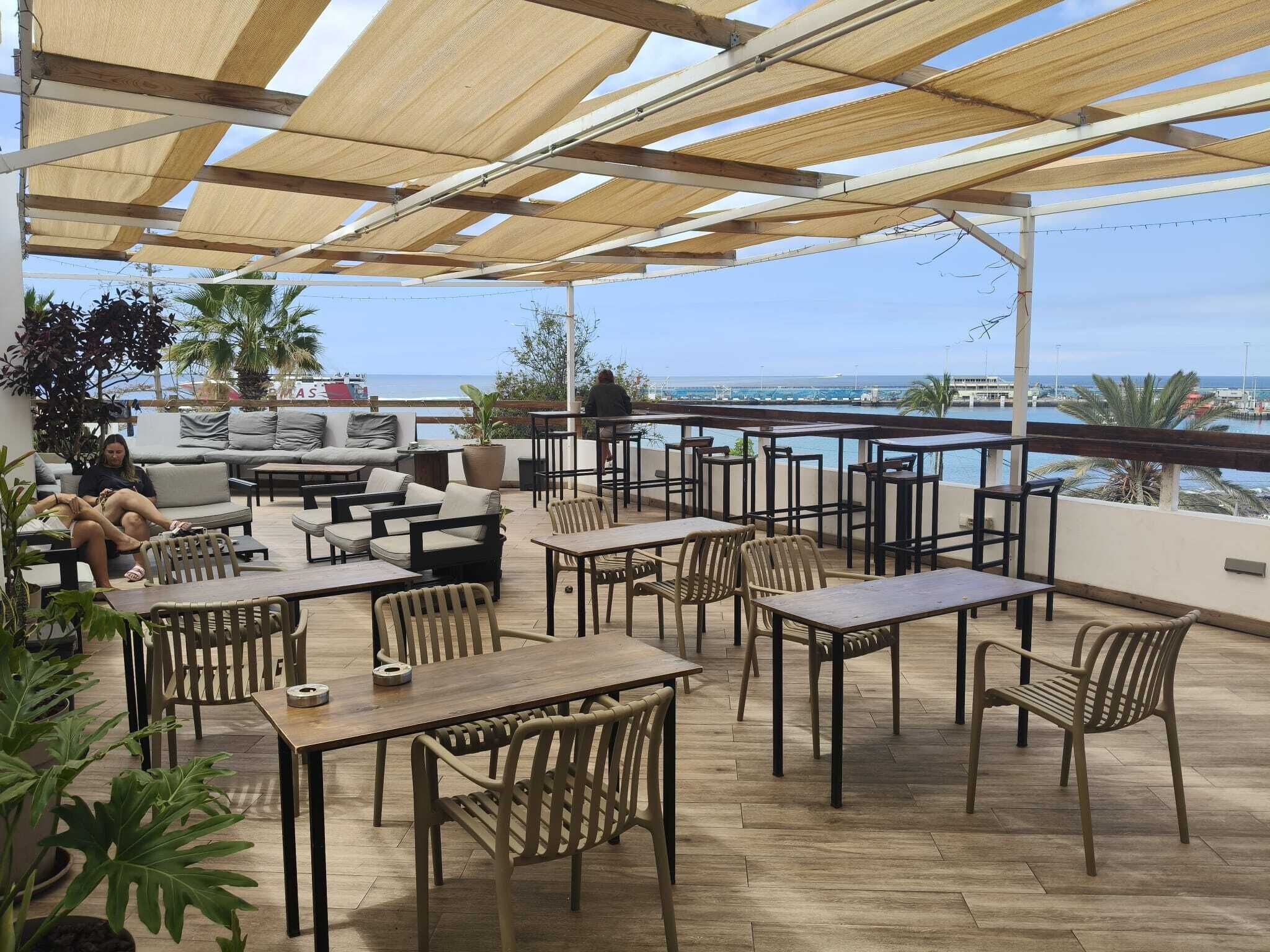 Un patio al aire libre con mesas y sillas, un sofá y vista al mar.