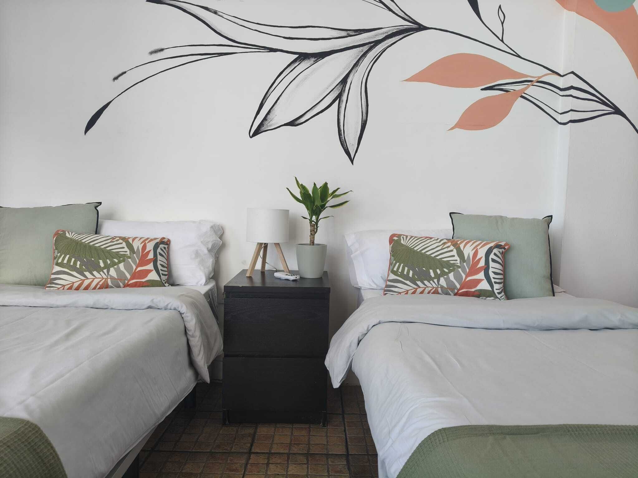 Un dormitorio con dos camas, una mesita de noche, una lámpara y una planta en maceta.