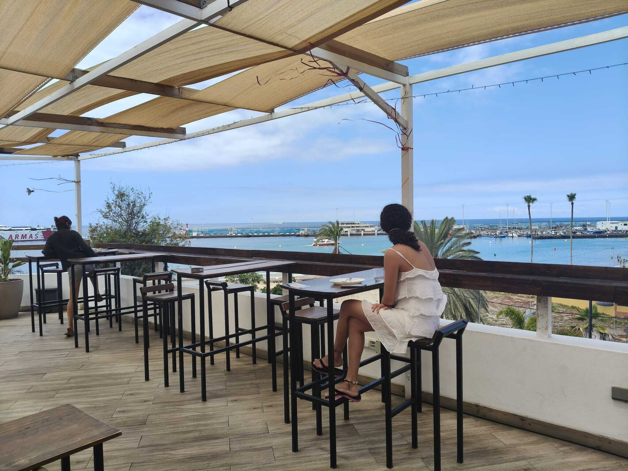 An outdoor seating area with tables and chairs, overlooking a marina and the sea.