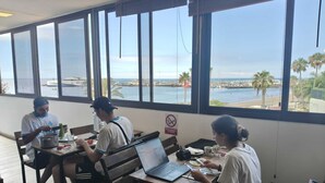 Un restaurante con amplios ventanales que ofrece vista al mar y a los barcos.