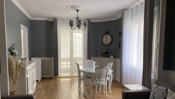 Un comedor con una mesa y sillas blancas, una araña y un reloj en la pared.