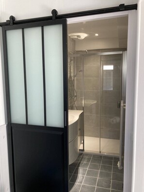 Uma casa de banho moderna com cabine de duche em vidro, lavatório branco e pavimento em mosaico escuro.