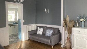 Un salón con un sofá gris, un aparador blanco y un florero con plantas secas.