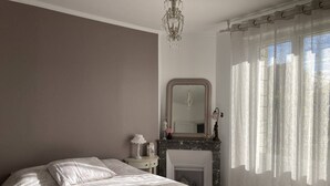 Un dormitorio con cama, mesita de noche, espejo, chimenea y cortinas translúcidas.