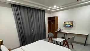 A hotel room with a bed, a desk, a chair, a TV, and a wardrobe. - Hotel Madhukta Inn (Somnath)