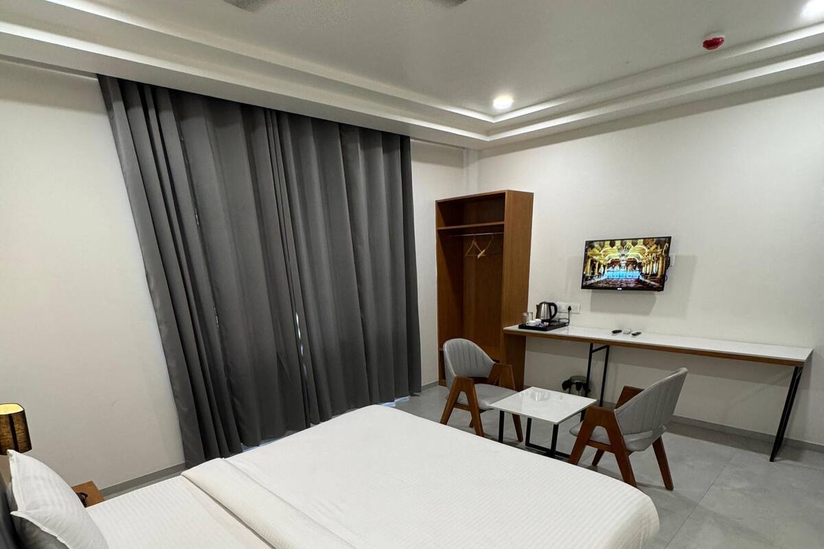 A hotel room with a bed, a desk, a chair, a TV, and a wardrobe.