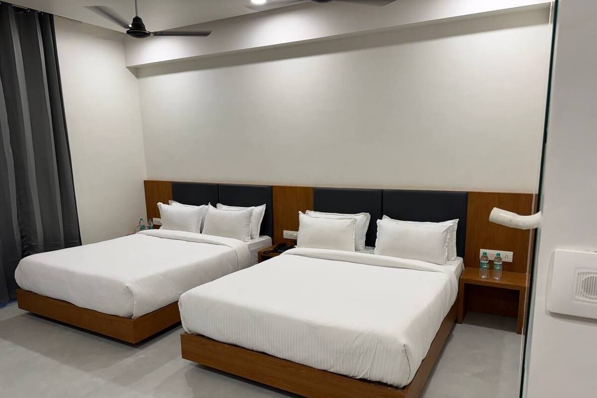 A hotel room with two beds, wooden headboards, white bedding, a nightstand with a phone and water bottles, and a ceiling fan.