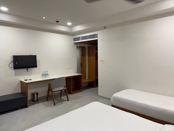 A hotel room with a bed, a desk with a chair, a TV mounted on the wall, and a wardrobe. - Hotel Madhukta Inn (Somnath)