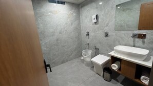 A modern bathroom with a marble wall, a white sink, a toilet, and a shower area. - Hotel Madhukta Inn (Somnath)