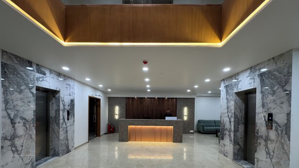 A modern reception area with a marble floor, wooden accents, and a central desk. - Hotel Madhukta Inn (Somnath)
