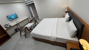 A hotel room with a bed, desk, chair, TV, and a small table with a lamp. - Hotel Madhukta Inn (Somnath)