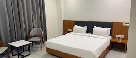 A modern hotel room with a large bed, a small table, a chair, and a nightstand with two bottles of water.