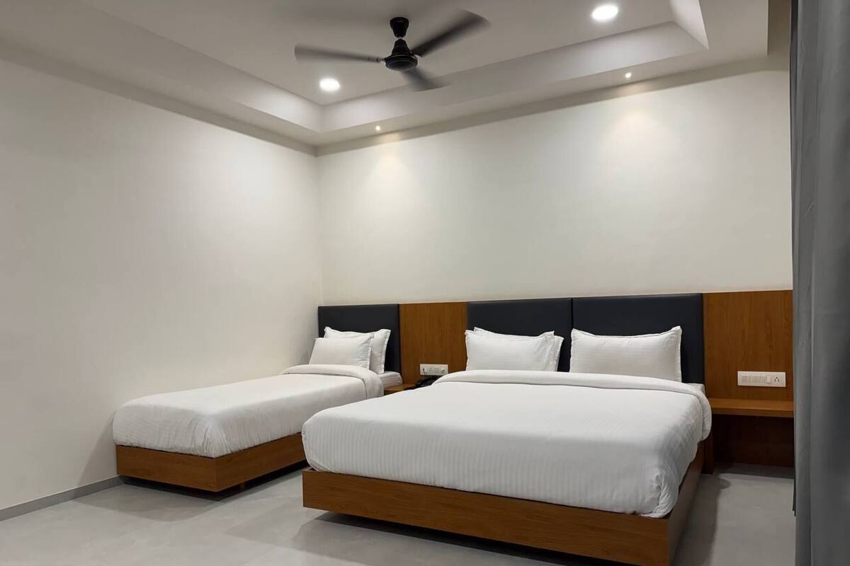 A modern bedroom with two single beds and one double bed, wooden headboards, and a ceiling fan.