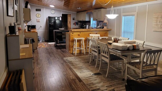 Une cuisine avec des meubles en bois, un coin repas avec des chaises blanches et un plafond en bois.