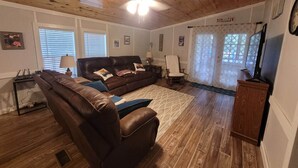 A living room with a brown leather sofa, a wooden ceiling fan, and a television on a wooden stand. - Lakefront on Nottely! Family retreat on single level with covered boat slip. (Blairsville)