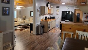 Une cuisine chaleureuse avec des meubles en bois, un coin repas avec une table et des chaises, et un salon avec un canapé et une table basse.