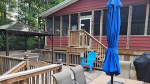 Une terrasse en bois avec des meubles d’extérieur, notamment une table et des chaises, et un espace abrité avec un parasol bleu.