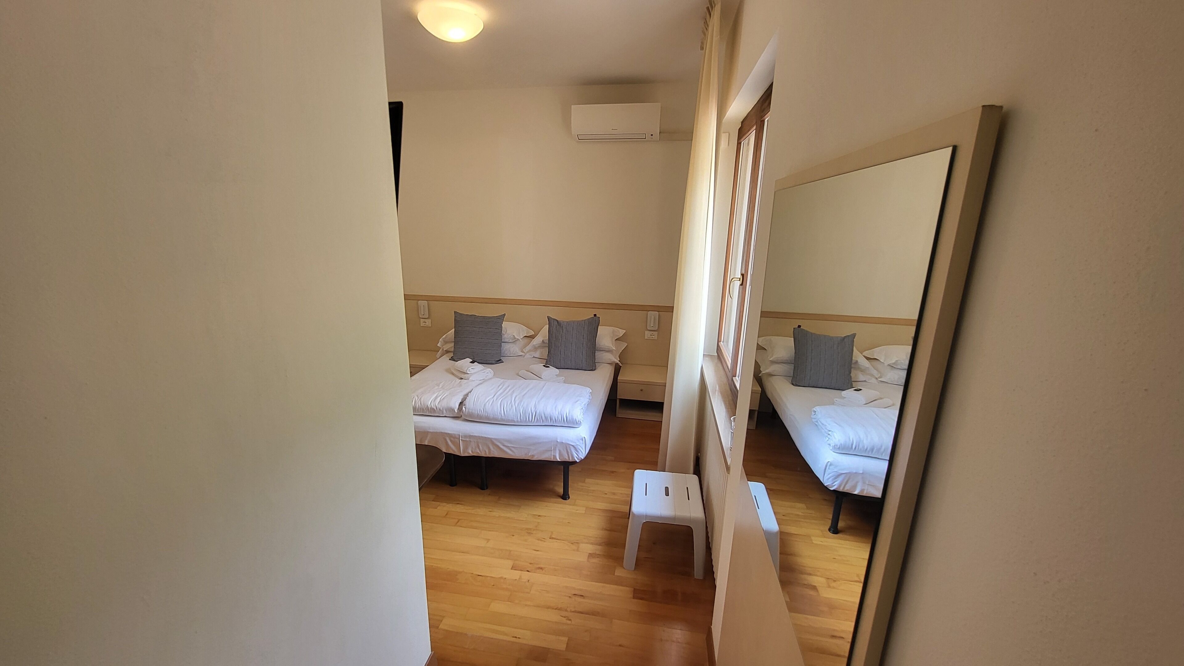 Ett hotellrum med två separata sängar, ett trägolv, en stor spegel och ett litet bord.