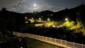 Une vue nocturne d’une zone riveraine, avec une clôture blanche, des lampadaires et des maisons en arrière-plan.