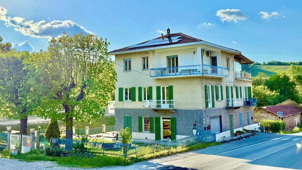 Un immeuble de deux étages doté d’un balcon, de volets verts et offrant une vue dégagée sur le paysage environnant.