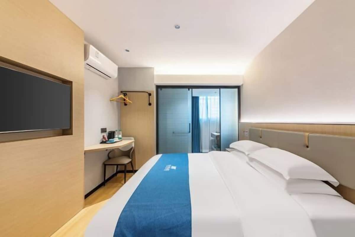 A hotel room with a bed, a desk, a chair, a TV, and a bathroom visible through a door.