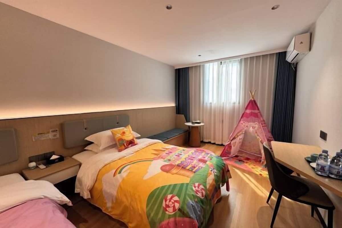 A hotel room with a bed, a desk, a chair, a nightstand, a bedside table, a lamp, a window with curtains, and a tent-like structure.