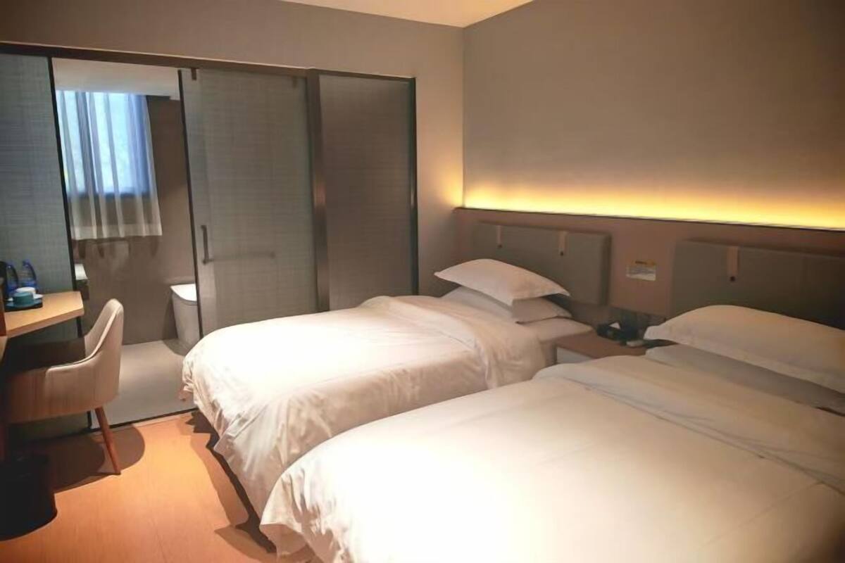 A hotel room with two beds, a desk, and a sliding door.