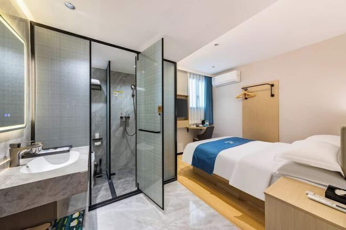 A hotel room with a bathroom, a bed, a bedside table, a nightstand, and a mirror.