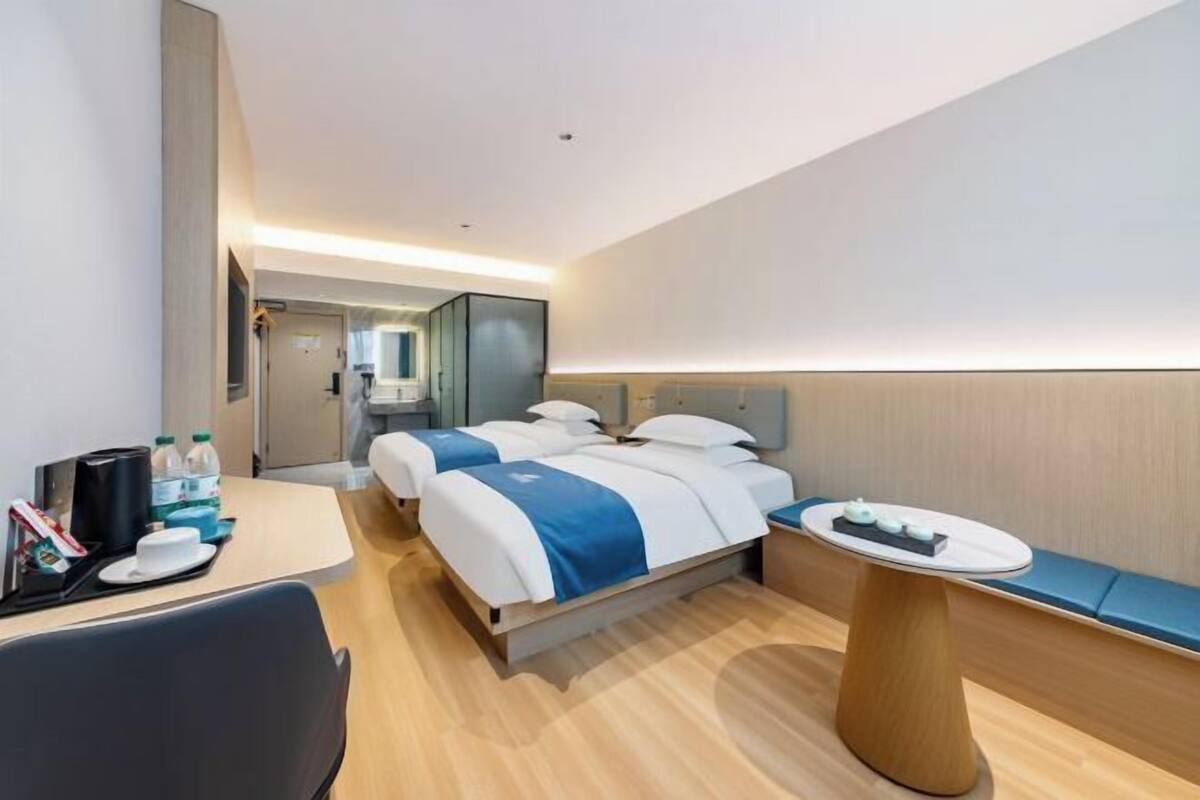 A hotel room with two beds, a desk, a round table, and a seating area.