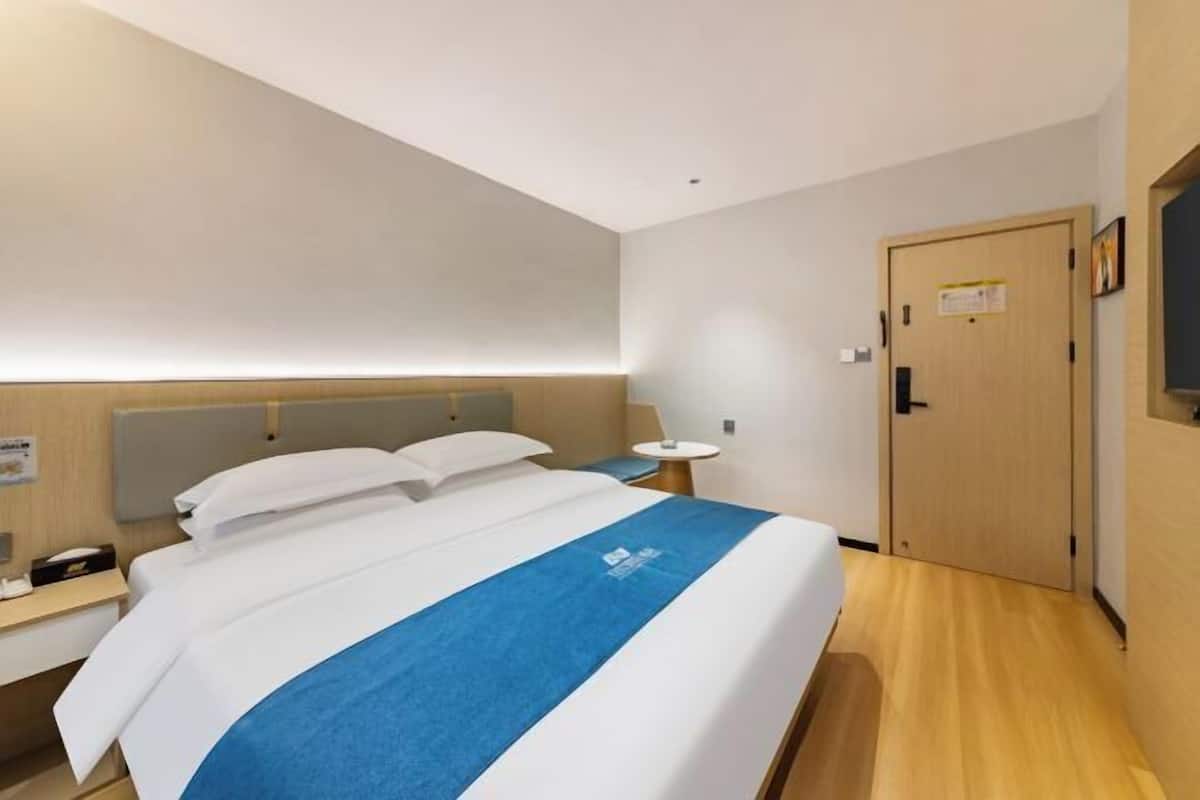 A hotel room with a bed, bedside table, lamp, and a door.