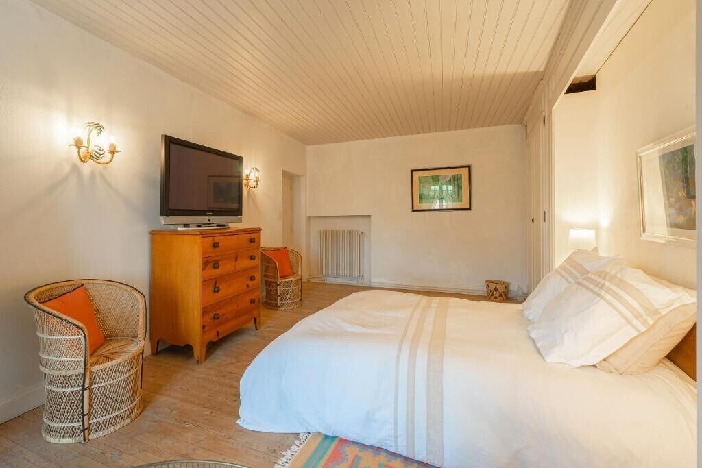Un dormitorio con cama, cómoda de madera, sillas de mimbre, televisor y un cuadro en la pared.