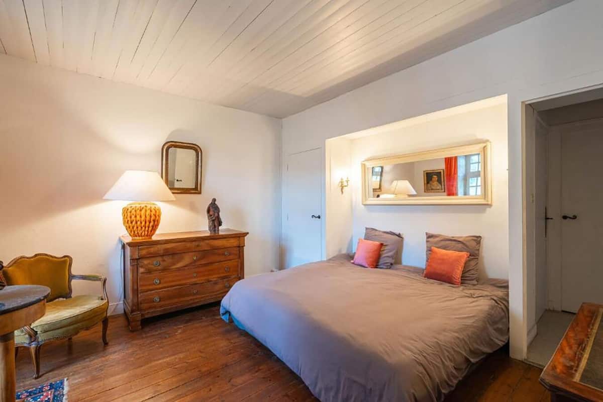 Ein Schlafzimmer mit einem Holzkasten, einem Bett mit vielen Kissen, einem Stuhl und einem Tisch.