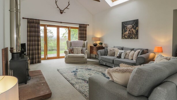 A cozy living room with a fireplace, a sofa, a chair, and a large window. - The Stables (Thornhill)