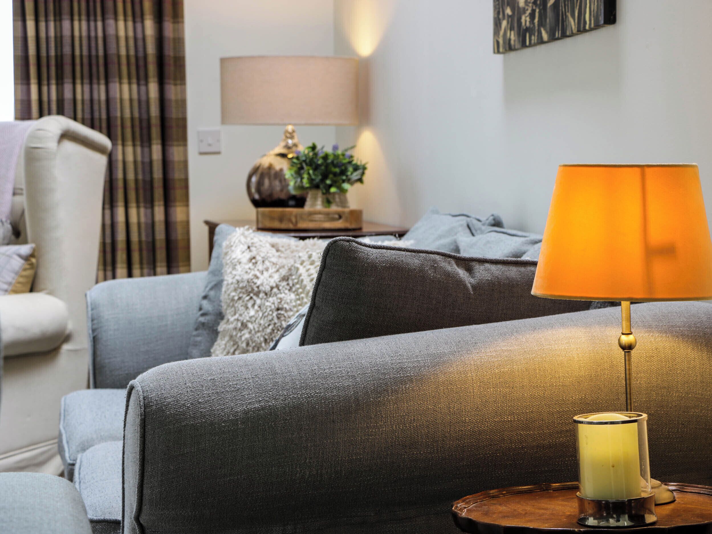 A living room with a grey sofa, a small table with a lamp, and a decorative vase.