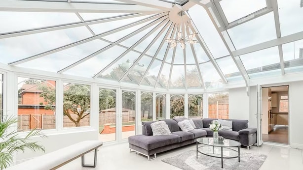A spacious conservatory with a modern grey sofa, a round coffee table, and a bench. - 6 Bed House - Sleeps 11 - Pets - Garden - Parking (Northwood)