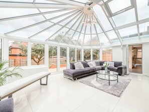 A spacious conservatory with a modern grey sofa, a round coffee table, and a bench. - 6 Bed House - Sleeps 11 - Pets - Garden - Parking (Northwood)