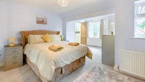 A bedroom with a bed, bedside tables, a radiator, a window, and a door leading to another room. - 6 Bed House - Sleeps 11 - Pets - Garden - Parking (Northwood)
