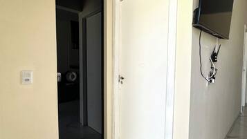 Un couloir avec une porte blanche, un téléviseur à écran plat fixé au mur et une prise de courant.