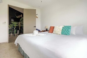 A hotel room with a bed, a desk, a chair, and a plant.
