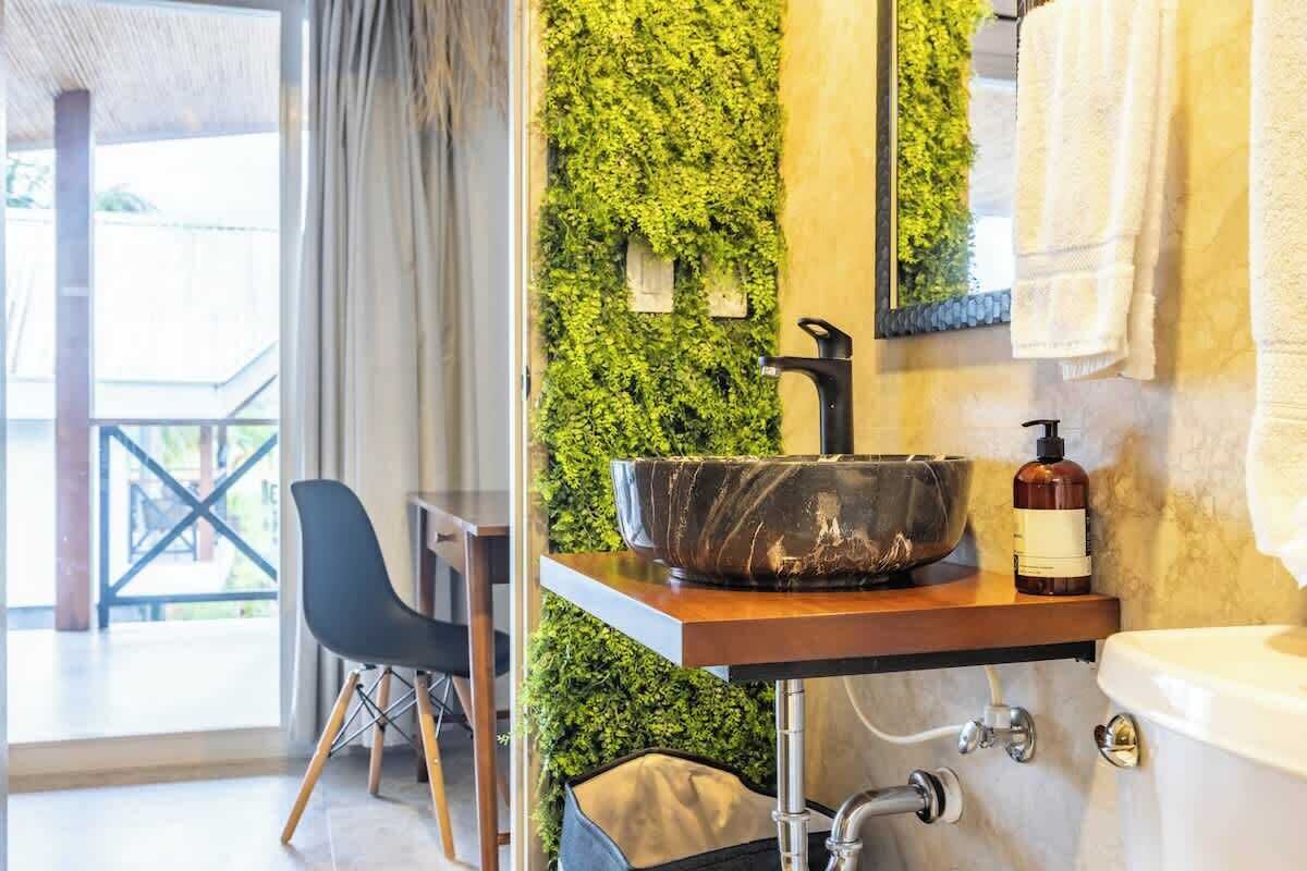 Une salle de bain avec un lavabo en marbre, un mur vert, une chaise et une vue sur l’extérieur.